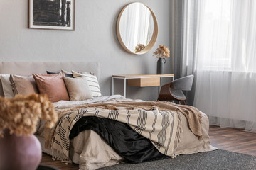 Elegant round mirror in wooden frame above fancy console table with flowers in vase in trendy...