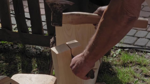 A traditional carpenter tapping an ax splits a large block of wood. He works outside during the event.