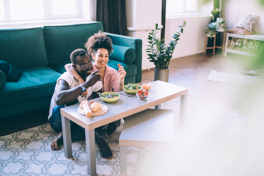 Multiracial Couple Watching Film And Laughing During Romantic Dinner At Home