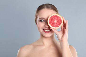 Young woman with cut grapefruit on grey background. Vitamin rich food