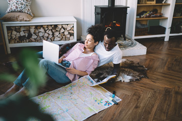 Ethnic couple using laptop and reading notes during journey preparation