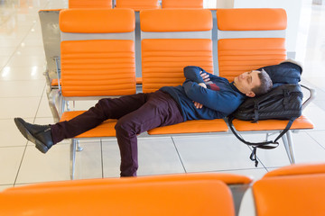 A 35-40 year old man sleeps on a bench while waiting for his flight at the airport. A passenger is waiting for his plane at the airport.