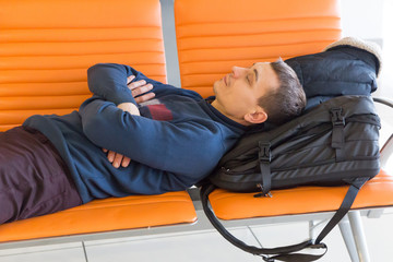 A passenger is waiting for his plane at the airport. A 35-40 year old man sleeps on a bench while waiting for his flight at the airport