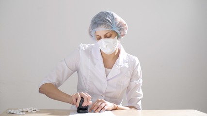 Female doctor in a medical protective mask and suit sits at a table and puts a stamp on the documents. Coronavirus or COVID 19. (2019-nCoV) 