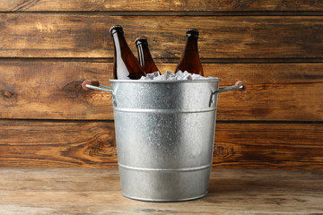 Metal bucket with beer and ice cubes on wooden background