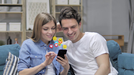 Smiling Young Couple Using Smartphone, Flying Smileys, Emojis and Likes