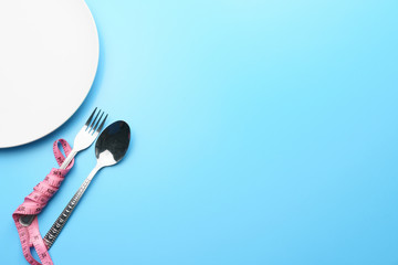 dieting and health care concept. top view the white plate with measure tape wrapped along fork and spoon on blue dine table. flat lay. free copy space for your text