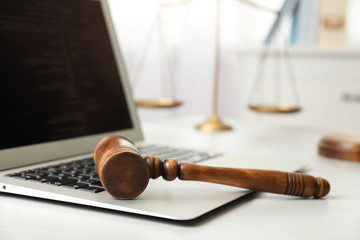 Laptop, wooden gavel and scales on white table, closeup. Cyber crime