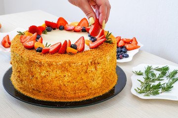 Girl decorates a freshly baked puff cake with fruits and berries: strawberries, blueberries and physalis Cooking. Strawberries, blueberries and physalis.