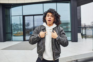 Handsome young man with curly black hair posing for the camera on the street against building