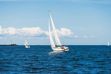 Fotobehang Zeilen White sloop rigged yacht sailing on a clear day. Lighthouse in the background. Cloudy blue sky. Bay of Riga, Baltic sea, Latvia  © Alex Stemmer