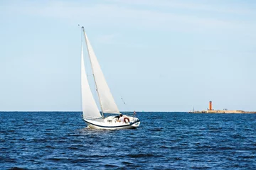 Foto auf Acrylglas White sloop rigged yacht sailing on a clear day. Lighthouse in the background. Cloudy blue sky. Bay of Riga, Baltic sea, Latvia © Aastels