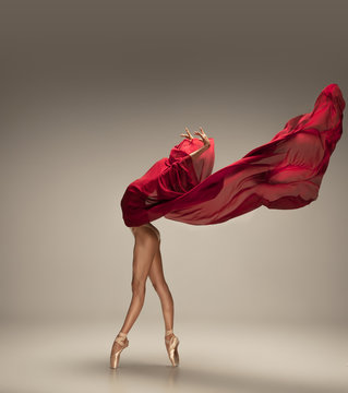 Free flight. Graceful classic ballerina dancing on grey studio background. Deep red cloth. The grace, artist, movement, action and motion concept. Looks weightless, flexible. Fashion, style.