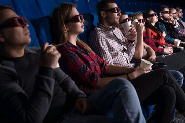 a group of young people of different sex, sitting in chairs in the cinema, watching a movie, eating popcorn. In glasses for 3D. Private screening of the film.