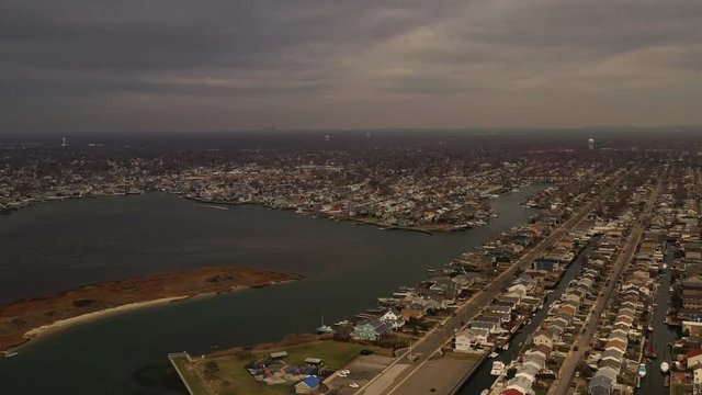 A high angle aerial view over the salt marshes in Freeport, NY. The drone camera pans left over the waterfront community & the horizon is in view. It is a cloudy day afternoon.