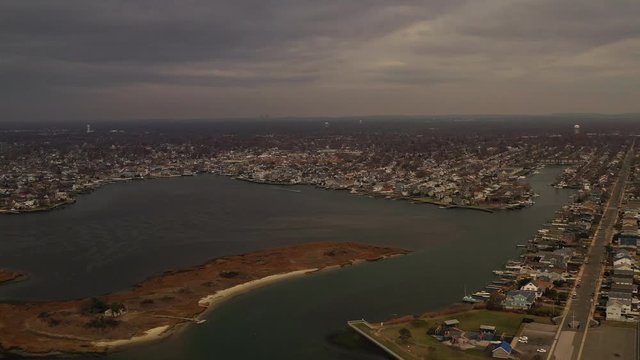 A high angle aerial view over the salt marshes in Freeport, NY. The drone camera pans left over the salt marsh on a cloudy day, with the waterfront community & the horizon in view.