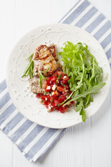 Grilled Pork Tenderloin with Tomato Salsa and Arugula. White wooden background. Top view. 