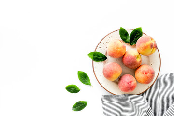 Summer lunch. Red peaches on white background with tablecloth and leaves top-down copy space