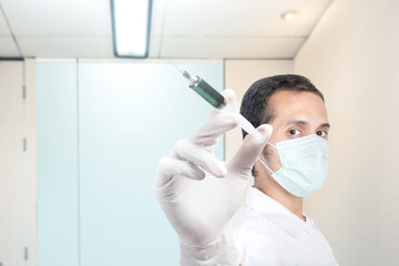 Asian man in protective gloves wearing a flu mask holding a syringe