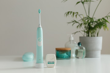 Fototapeta na wymiar Smart wireless ultrasonic toothbrush with dental floss standing in light bathroom. Innovative oral care technology. Beautiful blue color women's set. Concept of modern healthcare.