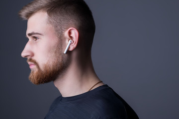 Closeup portrait of a young bearded guy of twenty-five years old, standing in profile. In wireless white headphones. Sporty style. Athletes headphone promotional photo