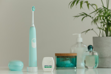 Smart wireless ultrasonic toothbrush with dental floss standing in light bathroom. Innovative oral care technology. Beautiful blue color women's set. Concept of modern healthcare.