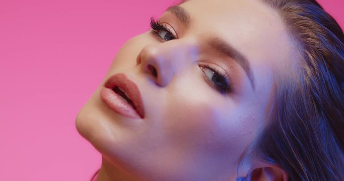 Fashion portrait of classy beautiful brunette. Model with smooth healthy skin and nude make-up strokes her smoothing skin with pleasure, looking at camera. Close up of girl in pink background.