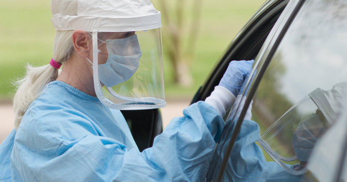 As Part Of The Operations Of A Coronavirus Mobile Testing Unit A Healthcare Worker Dressed In Full Protective Gear Swabs An Unseen Person Sitting Inside Of A Vehicle...