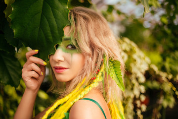 Dryad stands among the trees. Portrait of a beautiful girl with makeup on her face. Blinds a leaf...