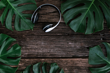 Flat lay creative frame of tropical nature leaves Monstera on rustic wood grunge background with retro Headphones, tropical jungle vacation and travel concepts. 