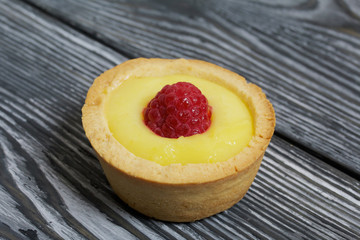Tartlets with lemon Kurd. Decorated with raspberries. They lie on black brushed pine boards.