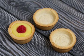 Naklejka na ściany i meble Tartlets with lemon Kurd. Decorated with raspberries. They lie on black brushed pine boards. Next to them are tartlets without toppings.
