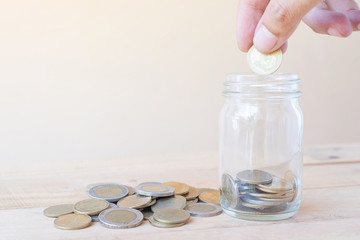 Fototapeta premium The hand hold coin and putting saving coins into glass with a pile of coinson wooden table - Investment, Business, Finance and Banking Concept