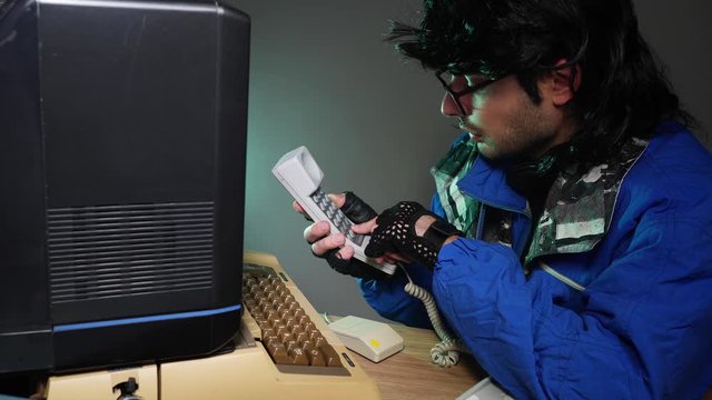 Computer Geek in glasses, dialing and talking on an old phone while using an old computer from 70s 80s retro concept