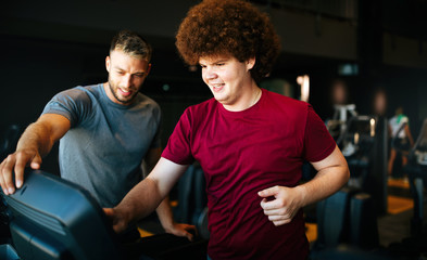 Overweight young man with trainer exercising in gym