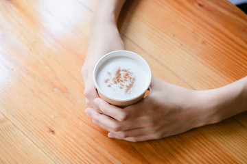 Hot drink in a craft plastic cup with a white cap in the hands of a young girl with a red manicure in a black coat close-up on the street in the fall afternoon.