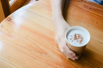 Hot drink in a craft plastic cup with a white cap in the hands of a young girl with a red manicure in a black coat close-up on the street in the fall afternoon.