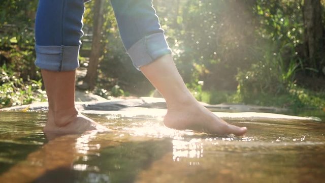 Bare feet of young woman splashing and kicking her legs in the water in the stream that flows slowly. Ladies enjoying vacation with nature at waterfall. Concept of lifestyle in summer vacation.