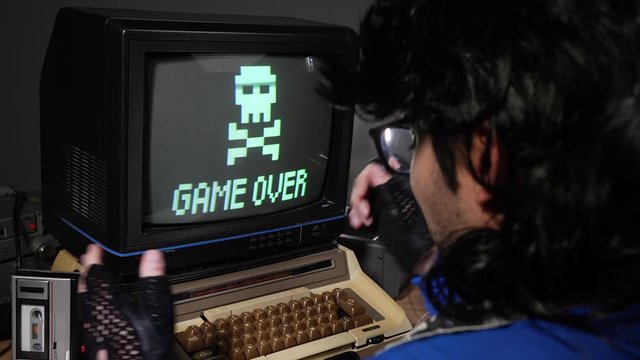 Upset, mad computer geek getting frustrated  and hitting old concept computer from 70s 80s because of loosing and seeing game over sign