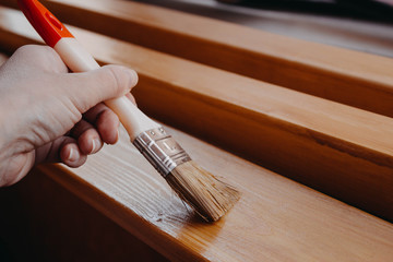 Female painter. Brush in a woman's hand , covering wooden planks and beams with varnish for interior work in the color of oak.