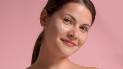 30s brunette woman with a cream smudge on face cheek. Self-care concept facial treatments for woman