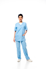 Full length view of african american nurse with hand in pocket smiling and looking at camera on white background