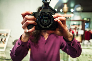 A close up and front view in selective focus of a man filming B roll, holding camera freely without tripod, with DSLR camera and lens reflections.