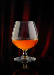 Glass with cognac on a red-black background with reflection