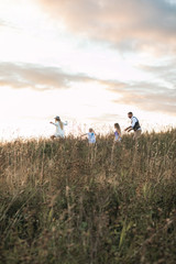 Happy family father, mother and two children daughters running and having fun together on nature summer field at sunset
