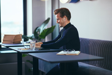 Businessman listening to music on earphones and using a laptop