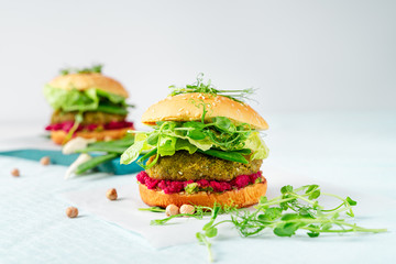 Two homemade vegan burgers with chickpea pattie, green peas and beetroot hummus on white background