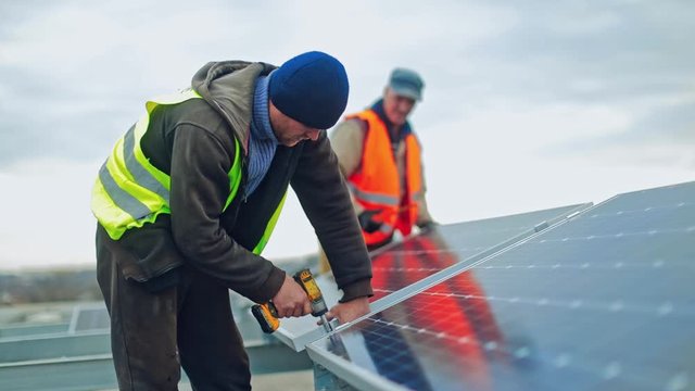 Technician connecting solar panel. Technicians working with electrical screwdriver installing solar panel to metal platform system