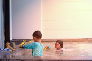 Fototapeta premium Boy and friend play dinosaur toy on poolside and play water in swimming pool in summer vacation with sun light and shade