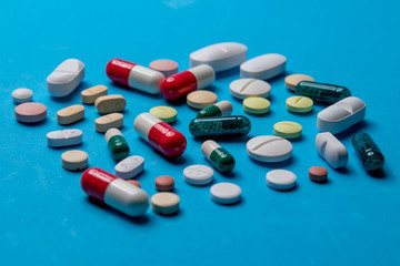 Assorted pharmaceutical medicine pills, tablets and capsules on blue background.